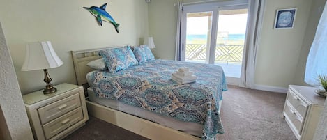 A bedroom with a bed, nightstand, and a view of the beach through the window.