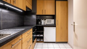Een compacte keuken met houten kastjes, een magnetron, een Bosch koelkast en een zwart aanrecht.