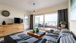 Een moderne woonkamer met een bank, salontafel, televisie en een balkon met buitenmeubilair.