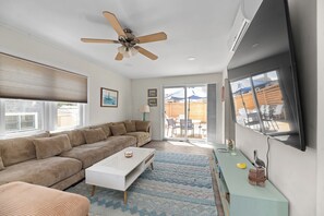 A living room with a sectional sofa, a coffee table, a TV, and a ceiling fan.