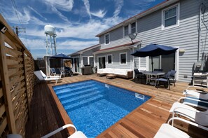 A swimming pool with wooden deck, lounge chairs, and a covered patio area.