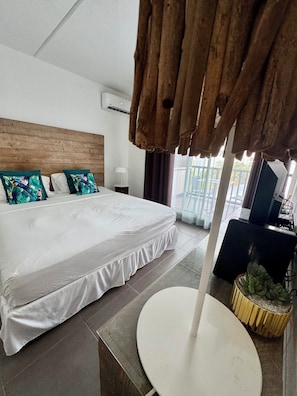 A hotel room with a large bed, a round table, a TV, and a view of the outdoors.