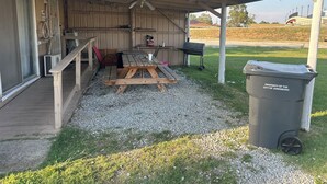 Ein überdachter Außenbereich mit Holztisch und -stühlen, einem Grill und einem Mülleimer mit der Aufschrift "Eigentum der Stadt Jonesboro".