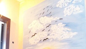 Seinämaalauksessa on kuvattuna auringonlasku, lentäviä lintuja, vihreä kaide ja taustalla näkyvä ovi.