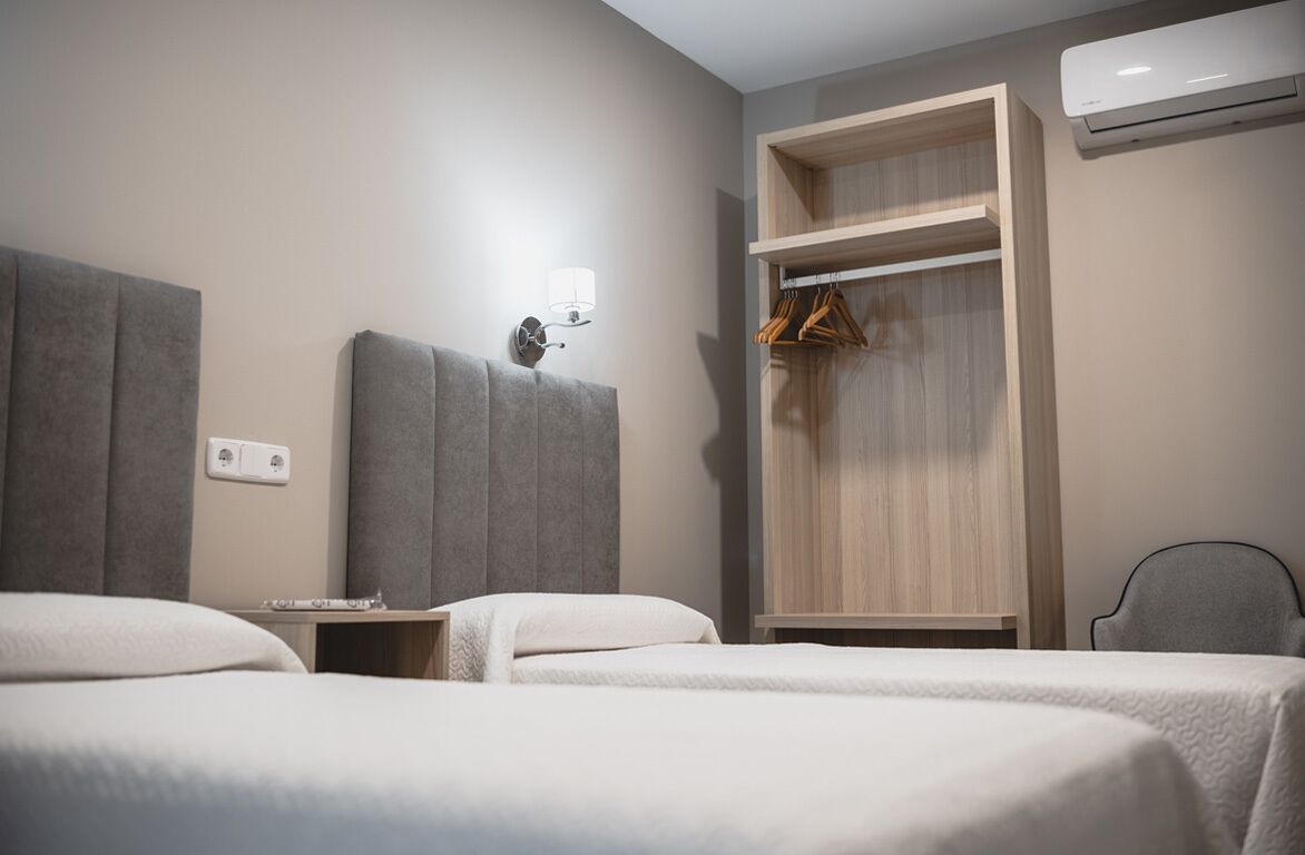 Une chambre d’hôtel avec deux lits, une armoire, une table de chevet, une lampe et un appareil de climatisation.