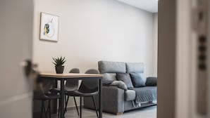 A modern living room with a grey sofa, a dining table with chairs, and a framed artwork on the wall.