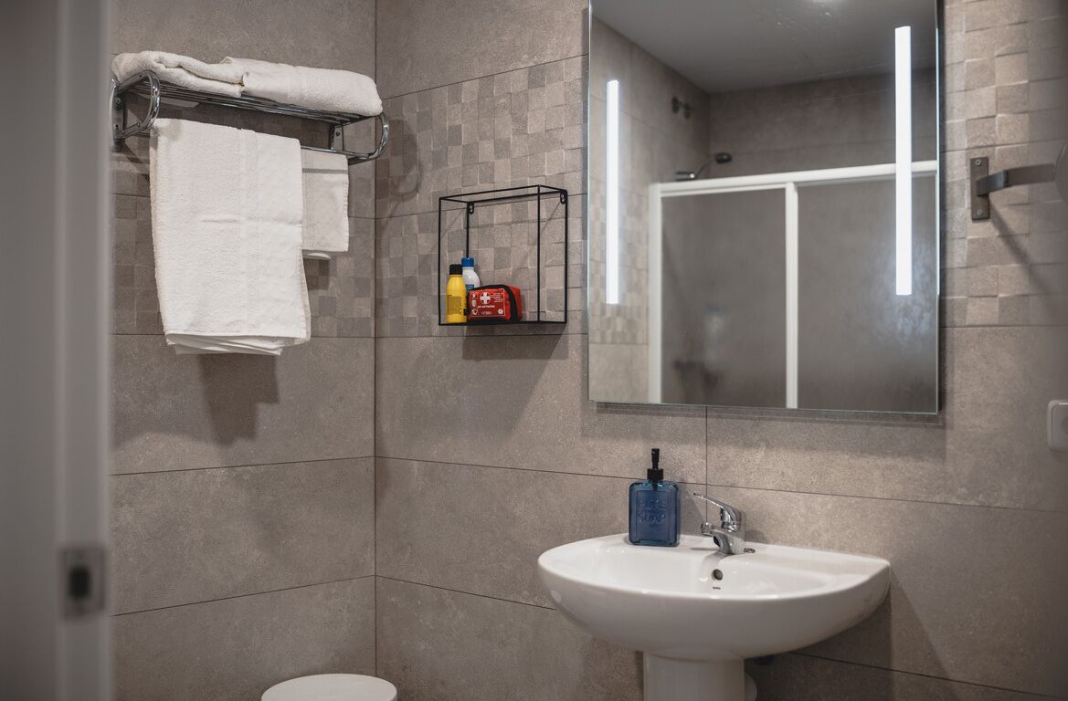 A modern bathroom with a white sink, a glass shower enclosure, and a towel rack with folded towels.