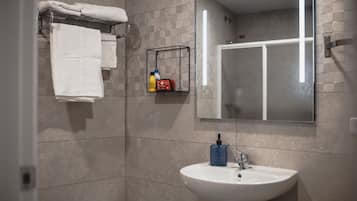 A modern bathroom with a white sink, a glass shower enclosure, and a towel rack with folded towels.