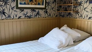 En säng med plats för en person, med vita sängkläder, en sänggavel i trä och en vägg med ett bambulövsmönster.