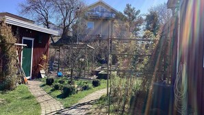 Ett bostadsområde med en gångstig som leder till ett trähus med en grön dörr, en metallkonstruktion och ett stort hus i bakgrunden.