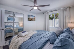 A bedroom with a bed, a ceiling fan, a window with curtains, and a painting on the wall.