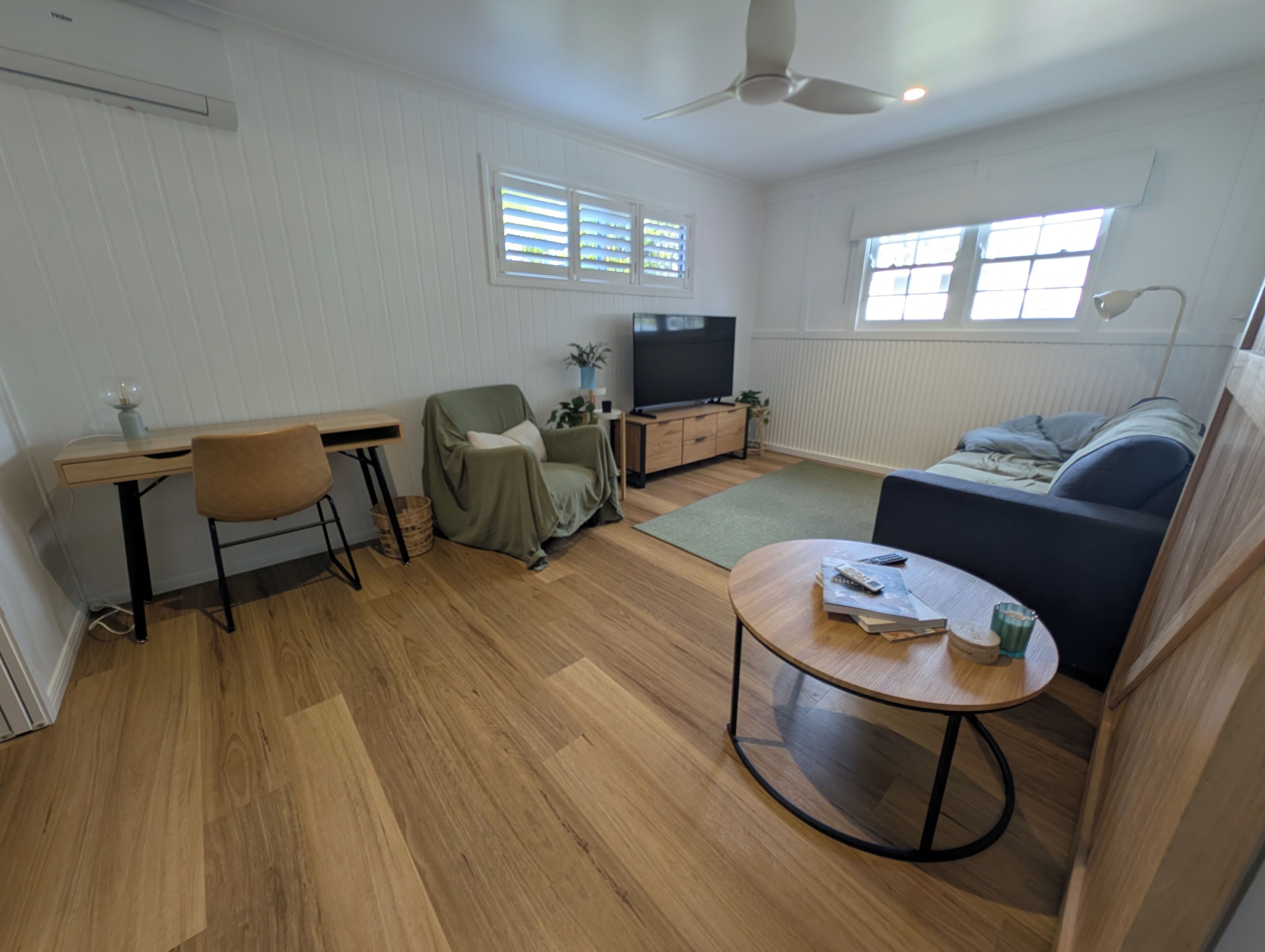 A modern living room with a flat-screen TV, a sofa, a coffee table, and a desk with a chair.