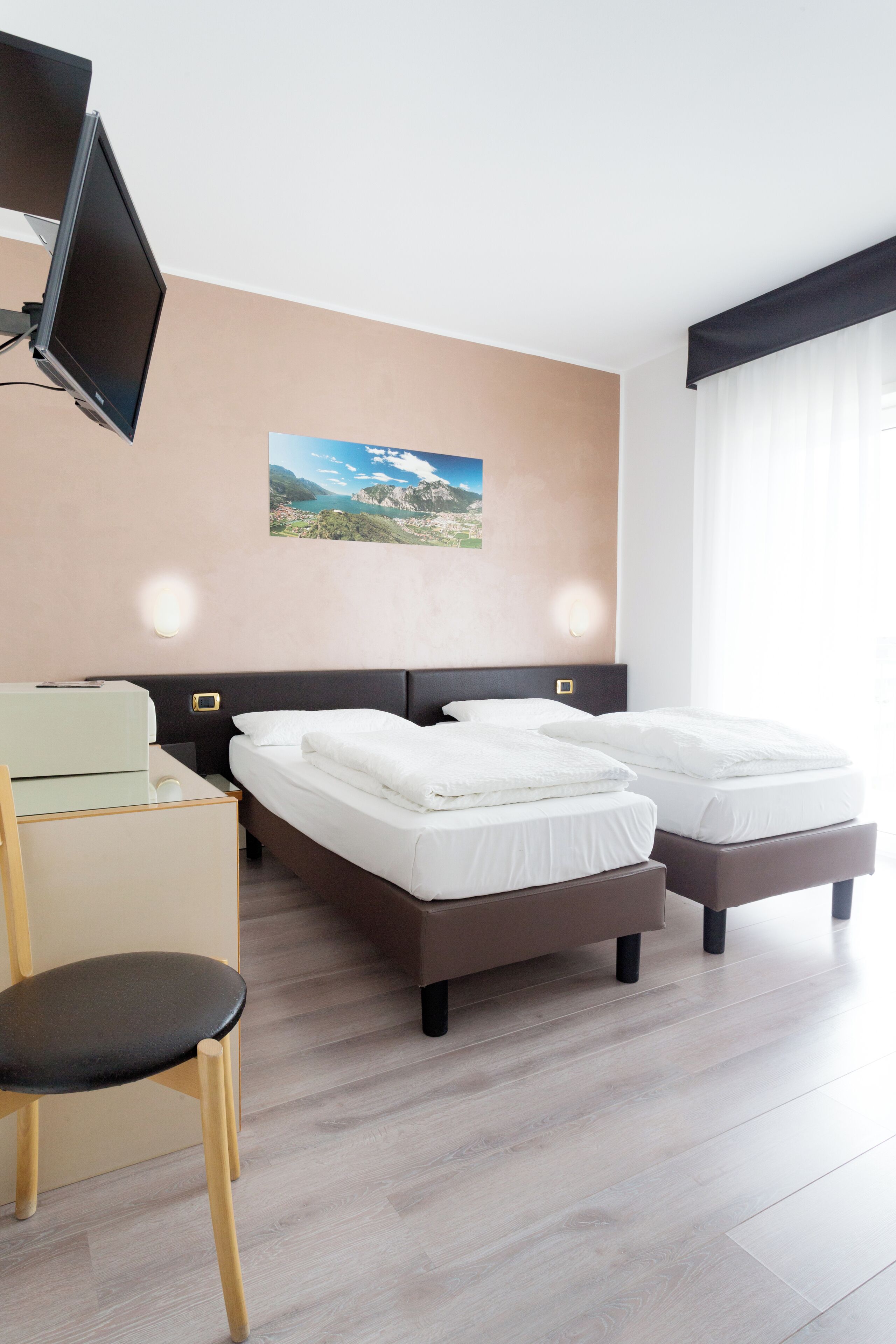 Une chambre d’hôtel avec deux lits, un bureau, une chaise, une télévision et un tableau au mur.