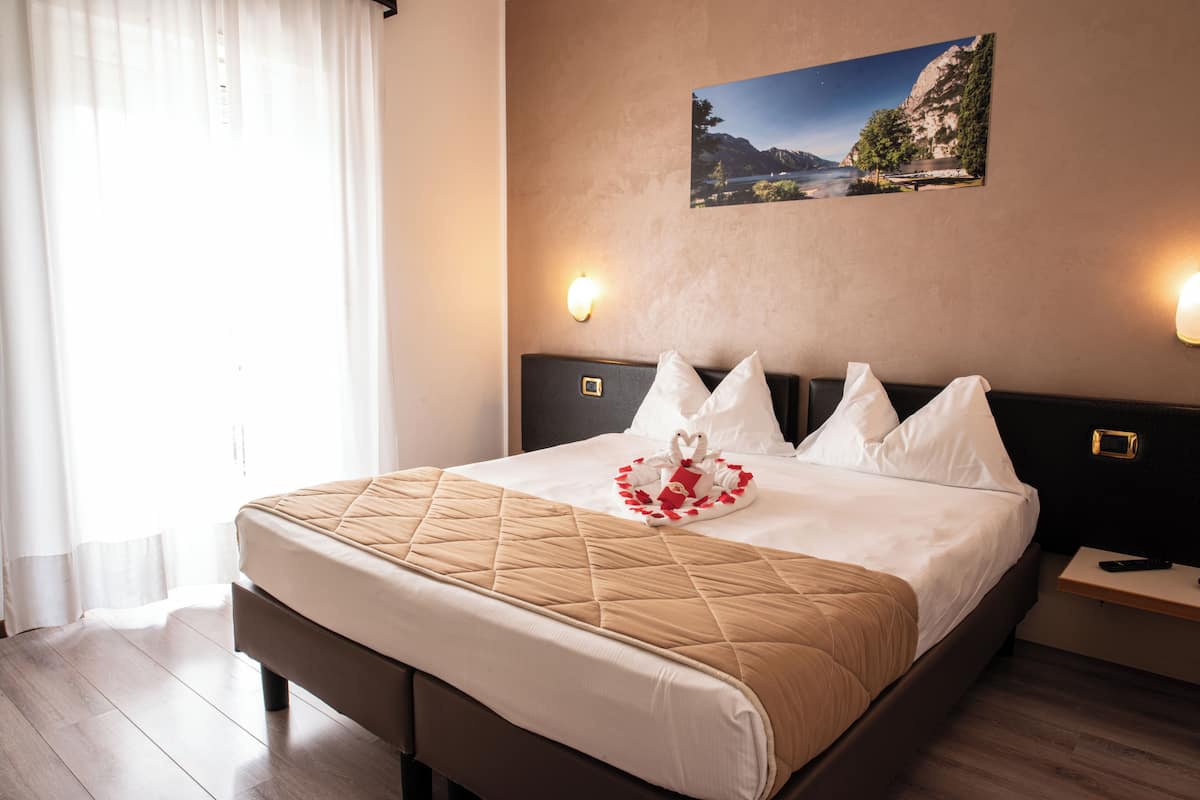 Un lit bien fait, avec une tête de lit matelassée, un tableau représentant un paysage accroché au mur, et deux lampes de chevet.
