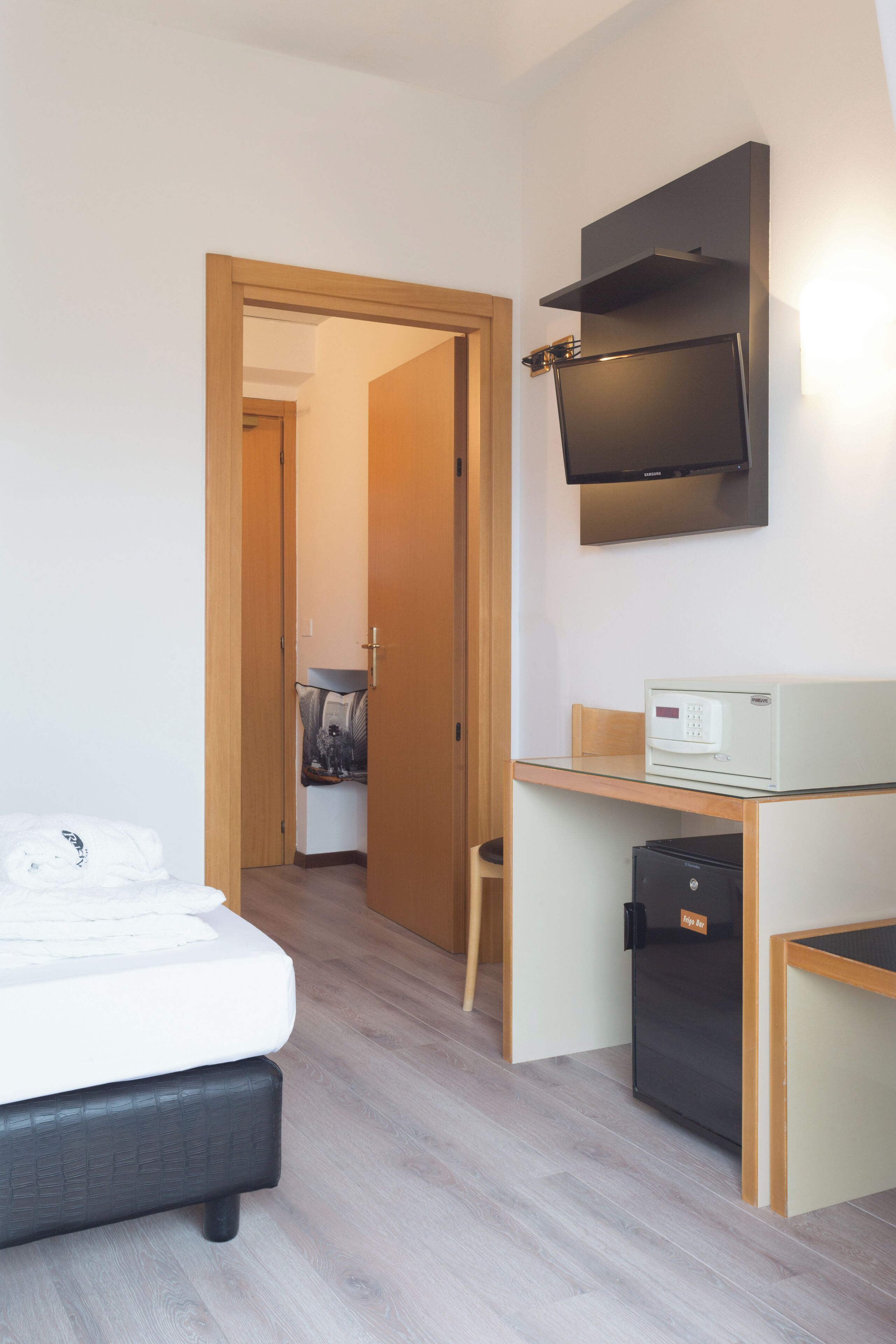 Una habitación de hotel con cama, escritorio con computadora, televisión y refrigerador pequeño.