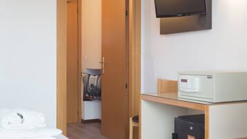 Una habitación de hotel con cama, escritorio con computadora, televisión y refrigerador pequeño.