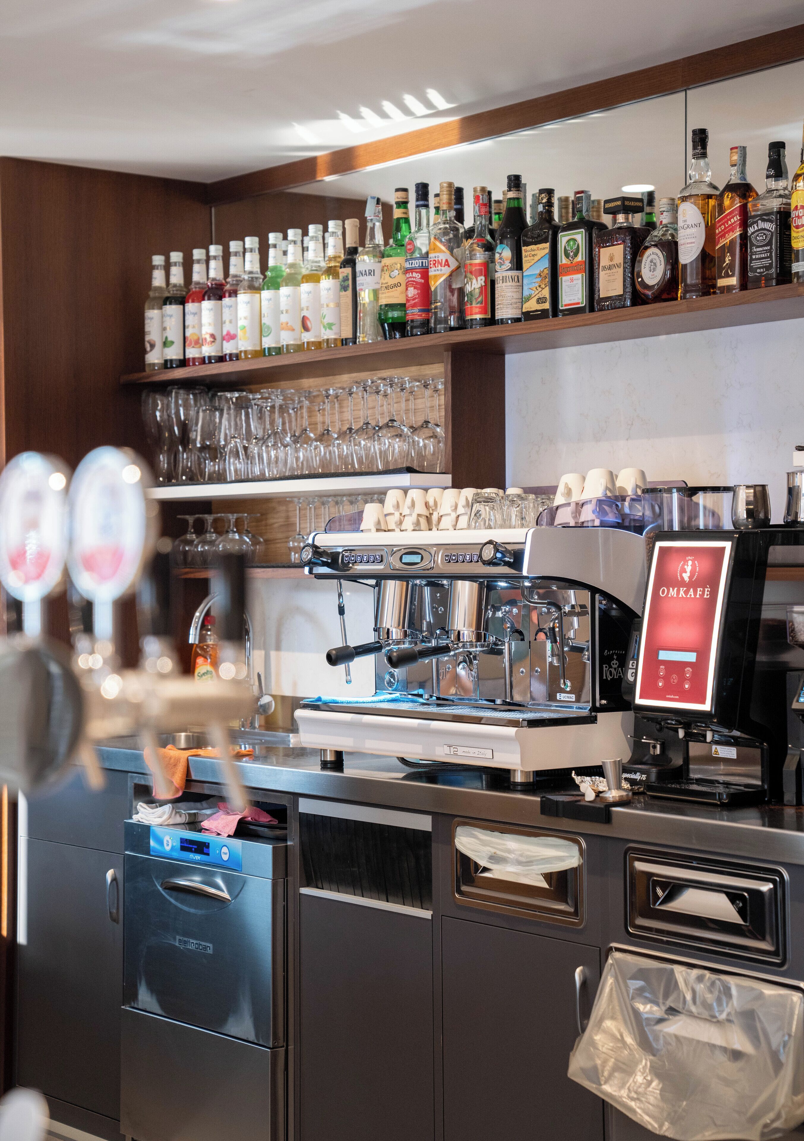 A bar area with a coffee machine, shelves of liquor bottles, and glasses.