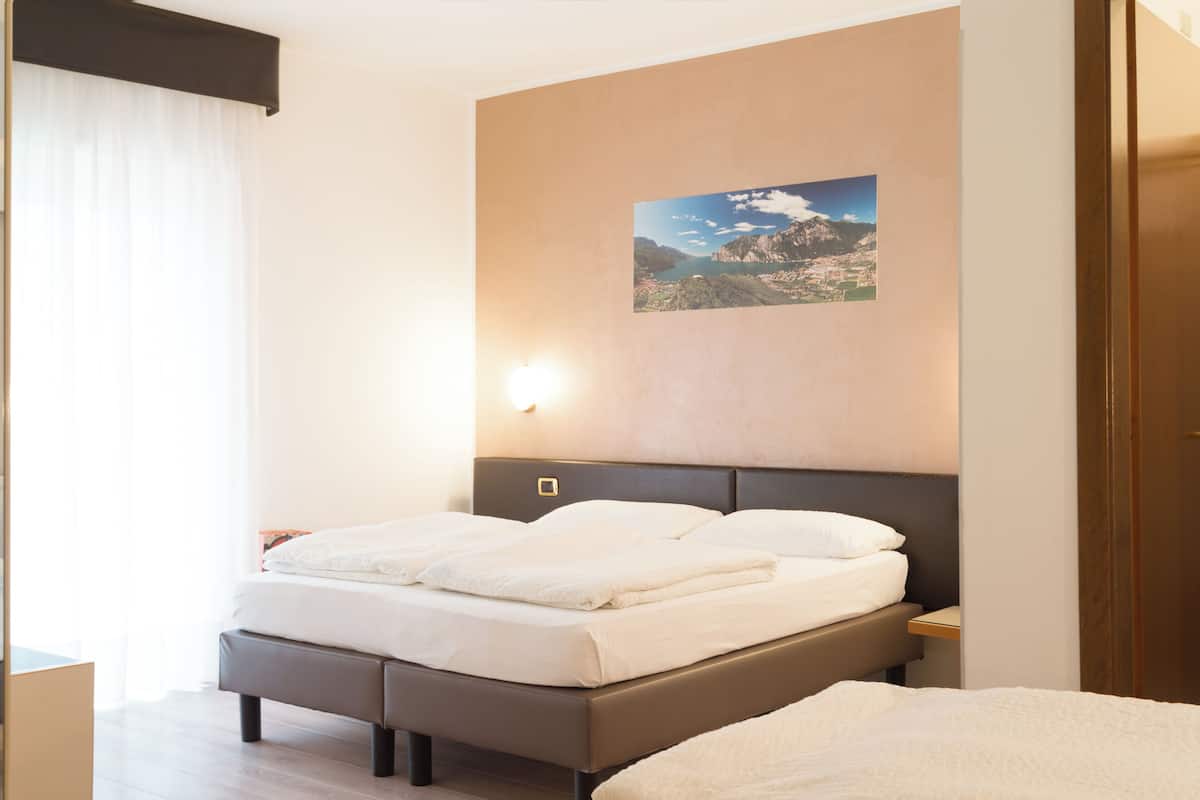 Une chambre d’hôtel avec un lit, une table de chevet, une lampe fixée au mur et un tableau représentant un paysage.