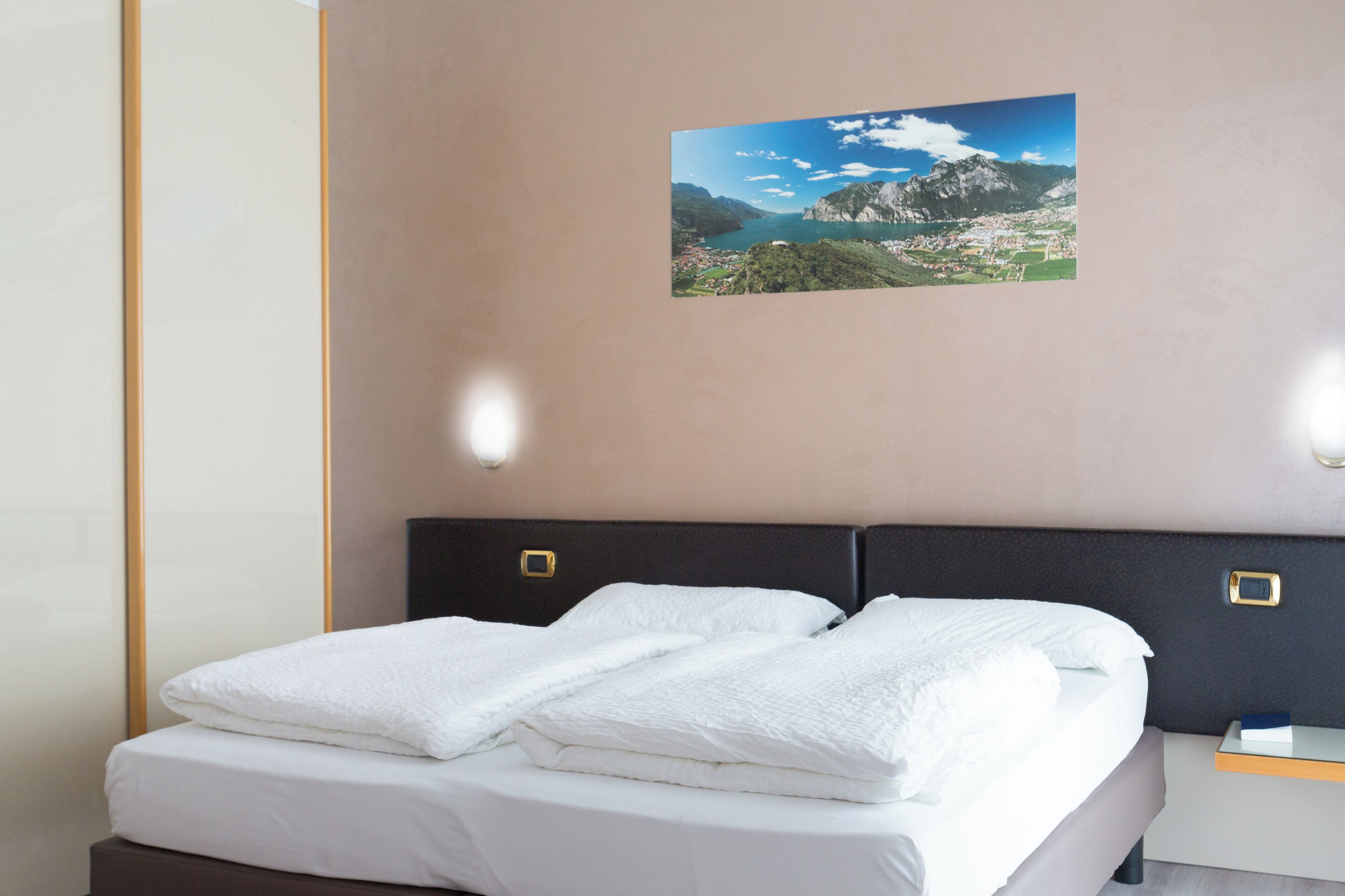 Habitación de hotel con una cama, una mesita de noche y un cuadro colgado en la pared de un paisaje montañoso.