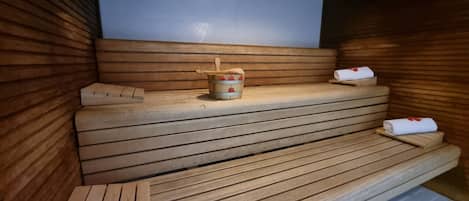 A sauna with wooden benches and a small wooden bucket with a lid.