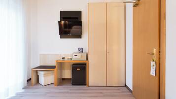 Une petite pièce comprenant une armoire en bois, un petit bureau avec un ordinateur et un réfrigérateur, ainsi qu’une porte sur laquelle est accrochée une note.