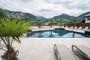 A swimming pool with lounge chairs and palm trees, surrounded by mountains.