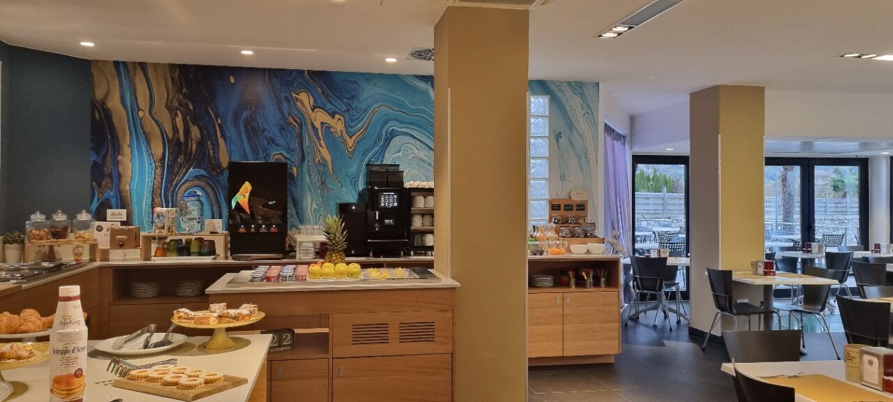 A modern breakfast area with a marble wall, coffee machines, and a buffet with pastries.