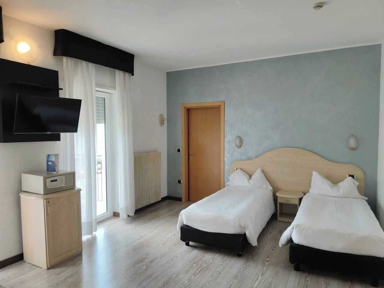 Camera d'albergo con due letti, una televisione, un piccolo armadio e una porta.
