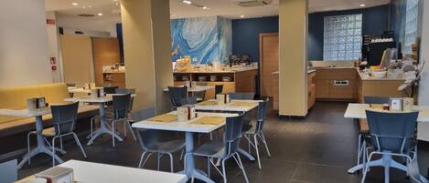 A modern cafe with multiple tables and chairs, a kitchen area, and a decorative wall.