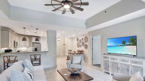 A modern living room with a sofa, coffee table, and TV. There is a kitchen area with cabinets and a dining table. - Located in the heart of the south end.  Close to everything (Saint Simons Island)