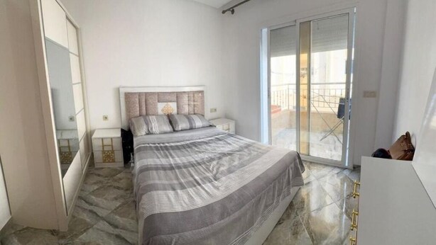 A bedroom with a bed, a nightstand, a wardrobe, and a sliding glass door leading to a balcony. - Family apartment near the sea (Martil)