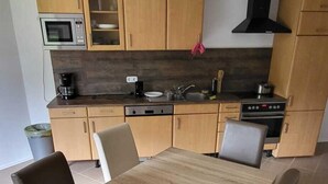 A modern kitchen with wooden cabinets, a built-in microwave, and a stove. - Pension Wolf (Hohe Börde)
