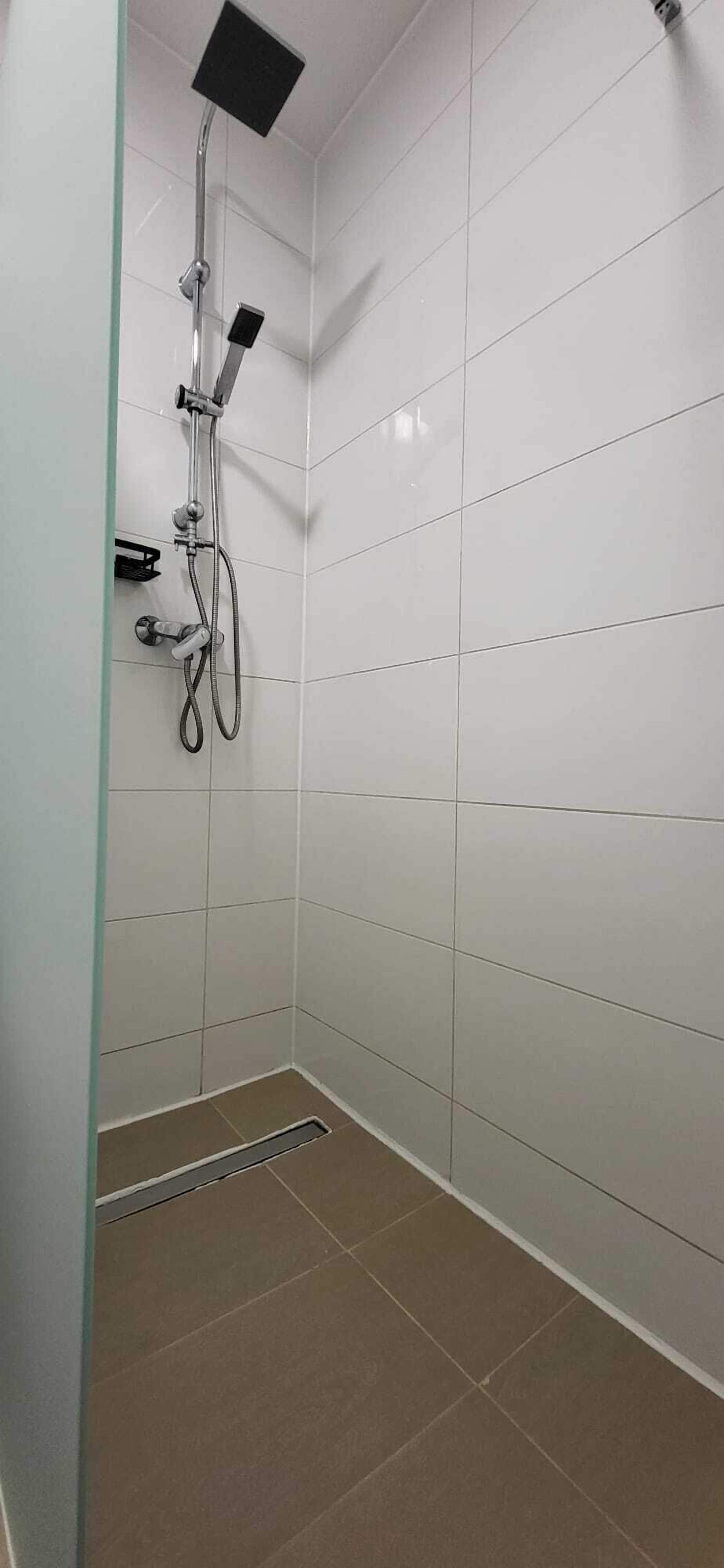 A shower with a handheld showerhead, a wall-mounted faucet, and a floor drain.