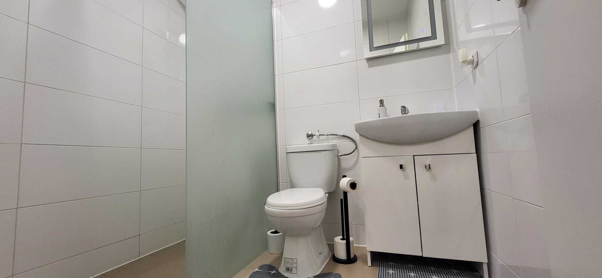 A small, clean bathroom with white tiles, a toilet, a sink, and a mirror.