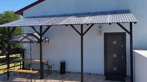 A covered patio area with a table and chairs, a trash bin, and a door. - Pension Wolf (Hohe Börde)