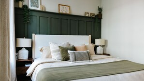 A neatly made bed with multiple pillows and a green throw blanket, flanked by bedside tables with lamps.