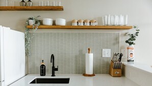 A kitchen with a white countertop, a black faucet, a wooden cutting board, a white soap dispenser, and a set of knives.