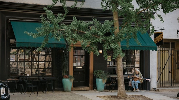 An Italian bakery with outdoor seating, a tree in the center, and a person sitting on a bench.