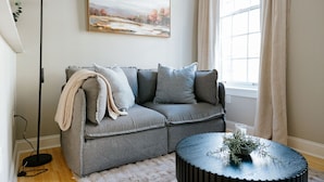 A modern living room with a grey sofa, a round coffee table, a floor lamp, and a painting on the wall.