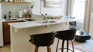 A modern kitchen with a central island, bar stools, a sink, and a dining area with a sofa.