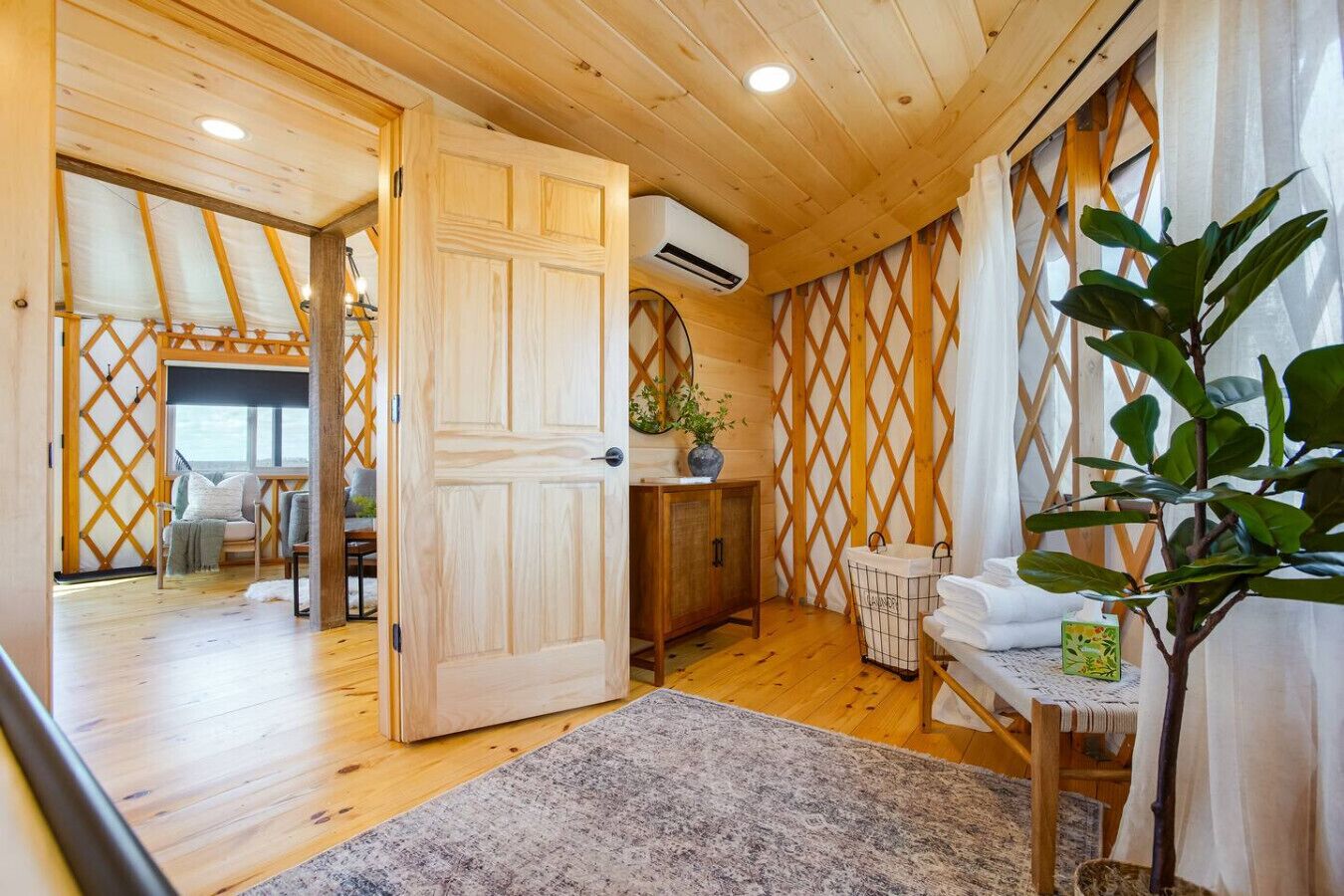 A wooden interior with a door leading to a room with a bed, a small table, and a plant.