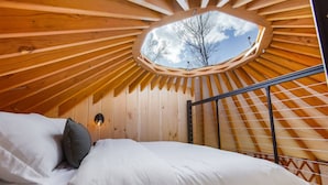 Een gezellige slaapkamer met een houten schuine kap en dakraam, met een bed met witte beddengoed en een grijs kussen.