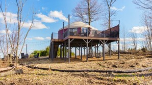 Een koepelvormig gebouw met een balkon op een verhoogd terras, omringd door bomen en een heldere lucht.