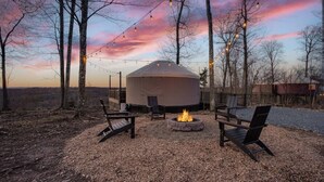 A yurt with a fire pit and seating, surrounded by trees and string lights. - Adventure Abode | Modern Yurt w/ Hot Tub, Bubble Dome + ADA Access (Reynoldsville)