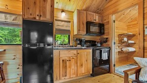 Eine kleine Küche mit Holzschränken, einem schwarzen Kühlschrank, einer Mikrowelle und einem Herd.