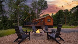 A cabin with a deck, surrounded by outdoor seating and a fire pit. - Hidden Creek Hideaway - Cozy Log Cabin w/ Hot Tub, Fire Pit & Scenic Views (Shippenville)