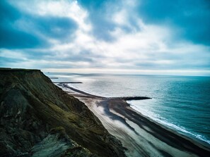 Un paisaje costero con un acantilado, playa y océano bajo un cielo nublado.