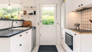 A compact kitchen with white cabinetry, a black countertop, a wooden cutting board, a sink, a stove, and a window with a view of greenery. - 6 Person Holiday Home in Dronningmolle (Dronningmolle)