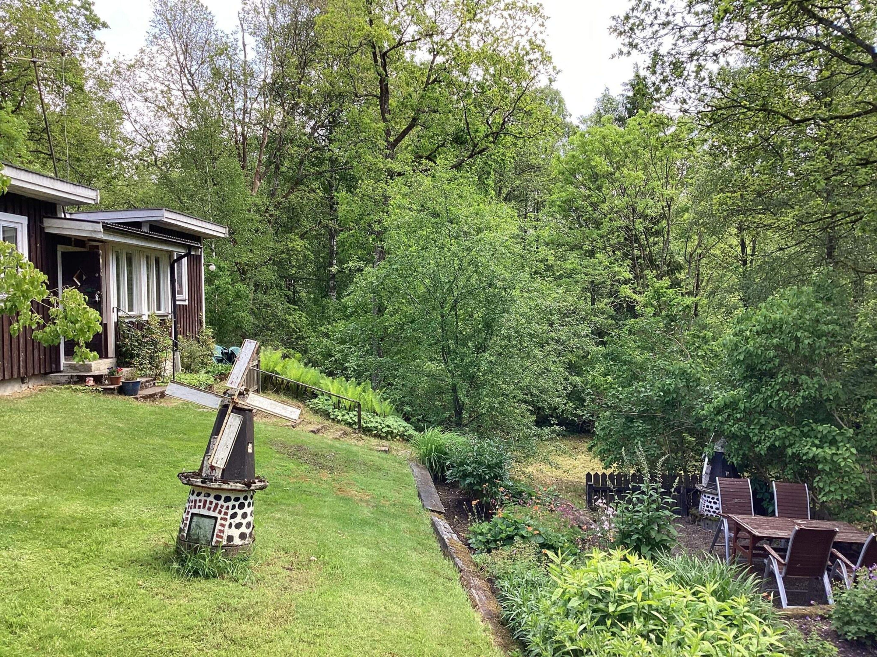 A residential property with a well-maintained lawn, a wooden deck, and a garden area with various plants and a small seating area with chairs.