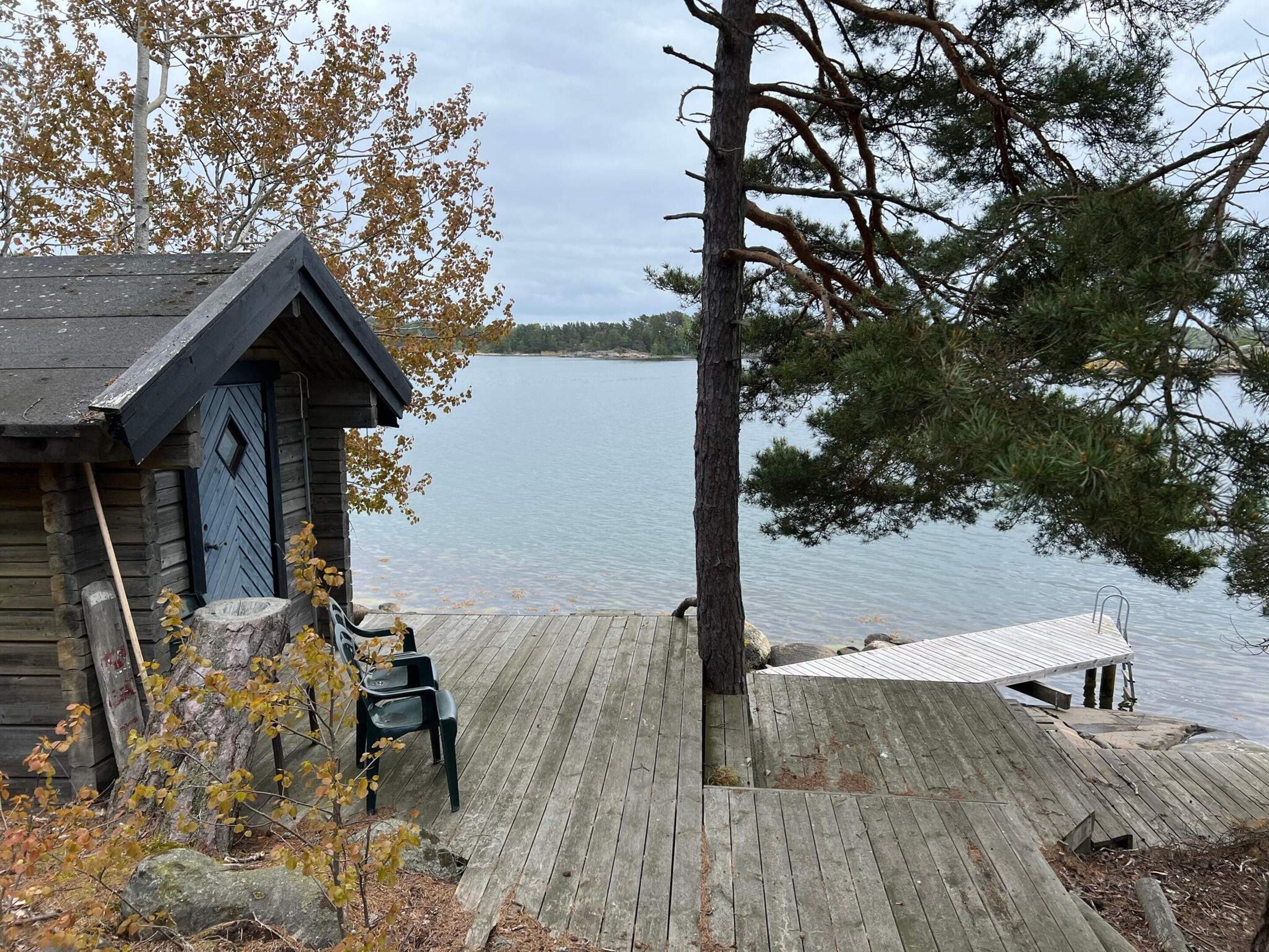 Una baita di legno con un pontile che si protende su un lago, circondata da alberi e foglie autunnali.